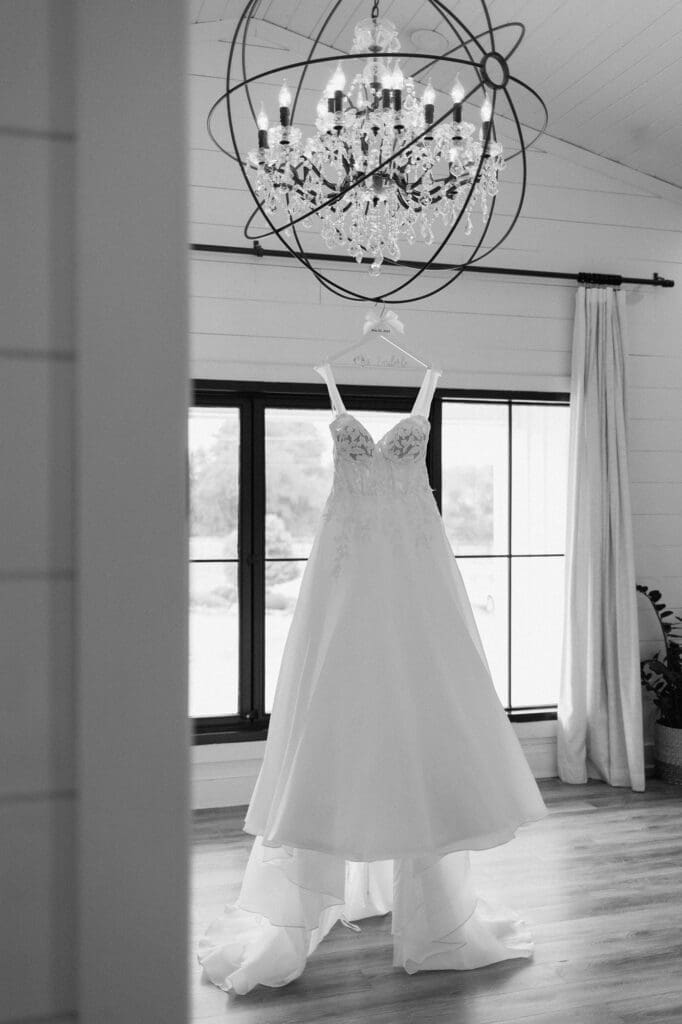 Black and white of the brides dress hanging from the chandelier in the bridal suite at The Farmhouse.