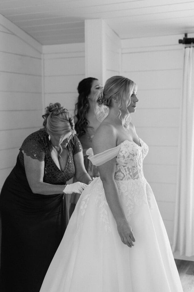 Black and white portrait of the brides mother buttoning up the brides dress in the bridal suite at The Farmhouse