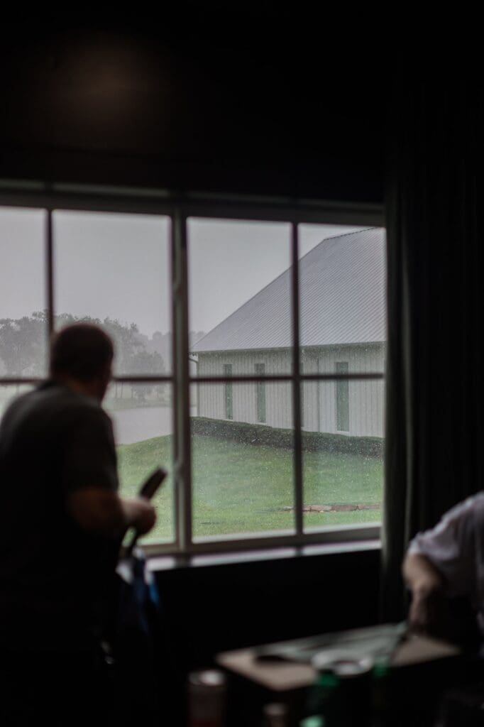 Shot of the window in the groom's suite showing the rain outside with the groomsmen blurry in the foreground.