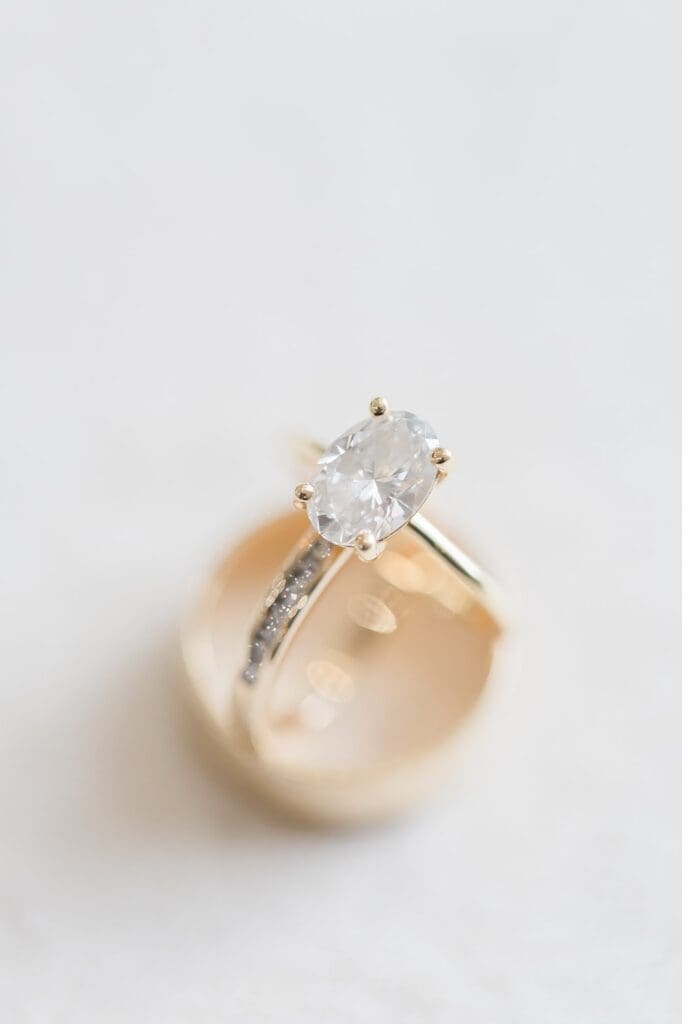 Top down up close view of engagement ring balanced by the groom and wedding flatlay.