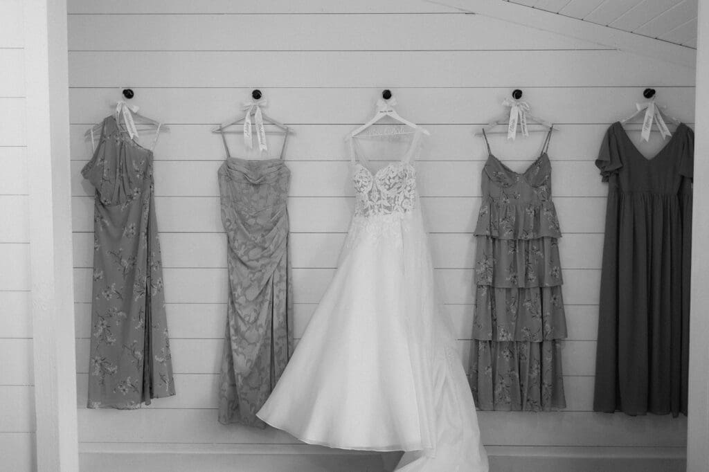 Black and white portrait of the bride and bridesmaids dresses hanging in the bridal suite at The Farmhouse.