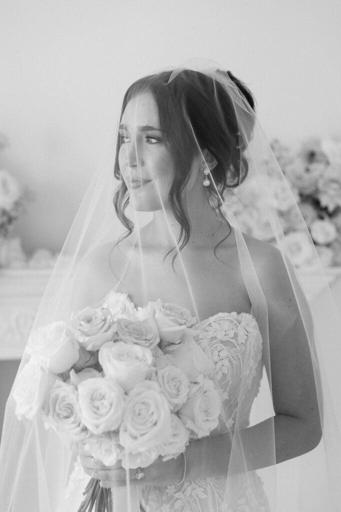 Black and white portrait of a bride smiling out the window with her veil covering her