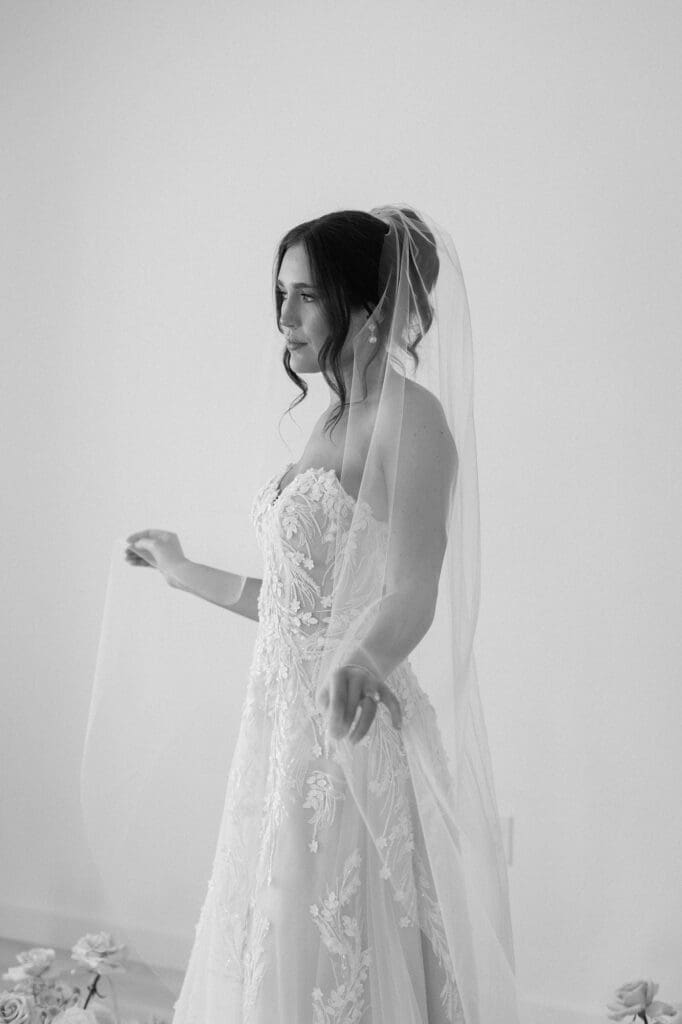 Black and white portrait of bride looking out the window and swaying back and forth with her veil