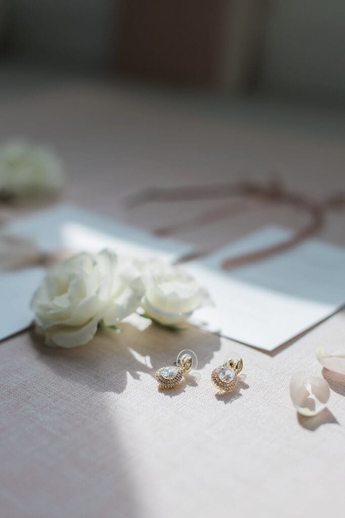 Light and shadows on a wedding detail flatlay. The earrings are the highlight of the image, shining in the sunlight