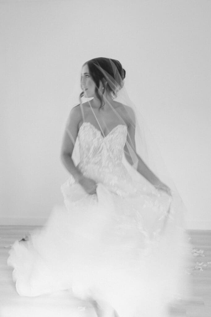 Black and white portrait of bride looking away running towards the camera. She is under veil and the bottom of her dress is slightly blurred conveying movement.