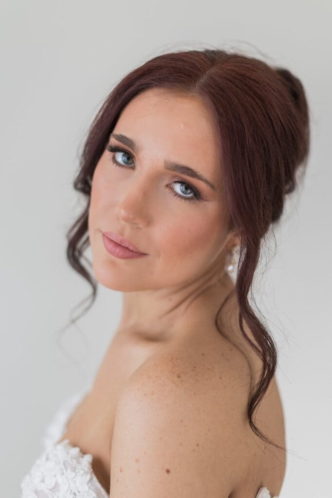 Beauty shots of bride looking back at the camera. Her hair is in an updo with her bangs curled framing her face. Her make up is a soft natural glam.