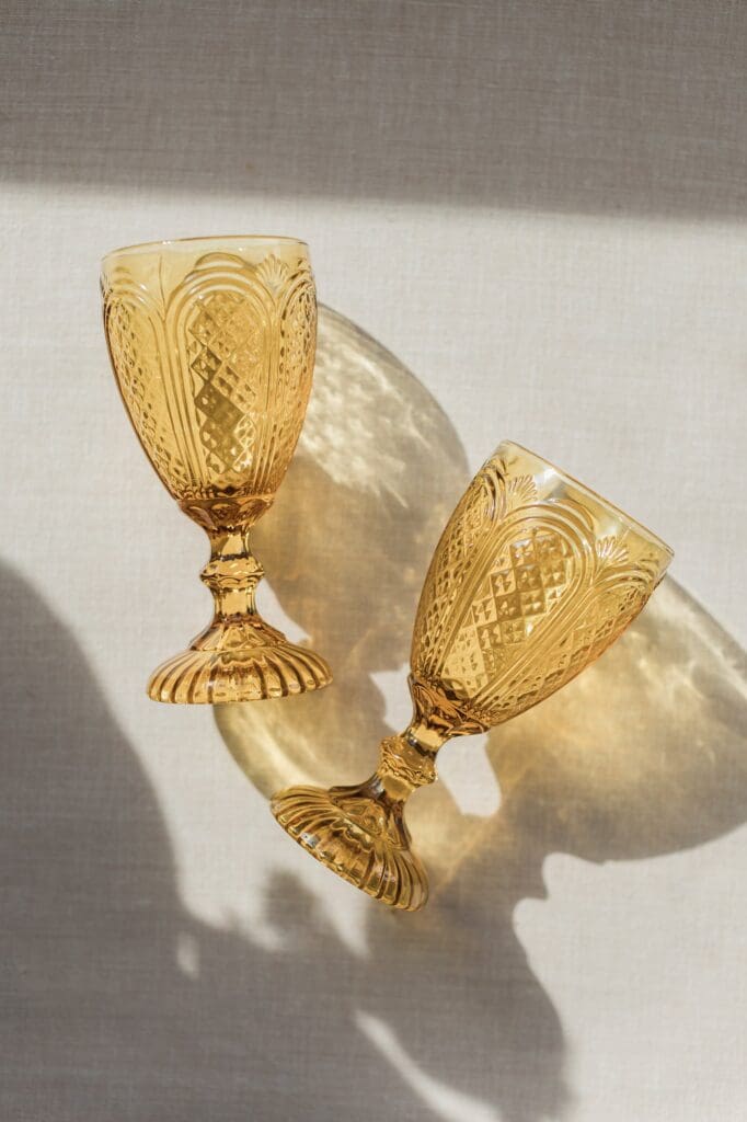 Light casting shadows and reflections of a textured yellow water goblet for a wedding flatlay
