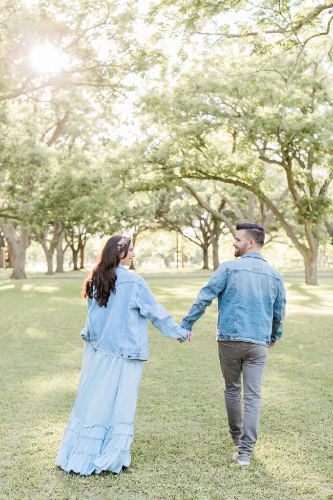 Bride and groom smiling at each other as they walk away during their engagement session at the orchard at caney creek