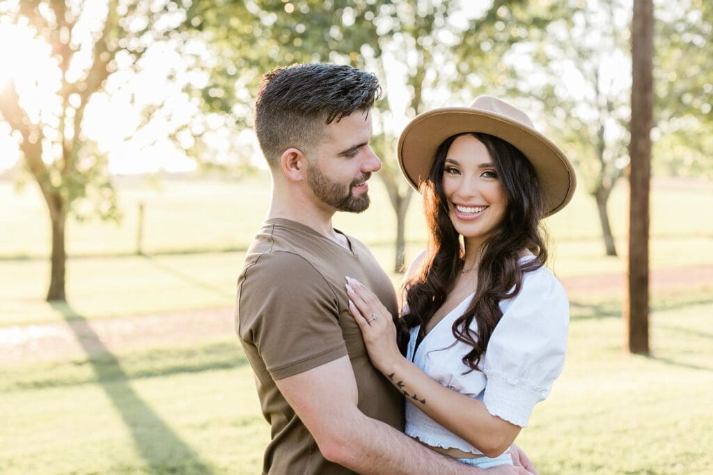 Bride laughing at camera while the groom smiles at her during their engagement session at the orchard at caney creek
