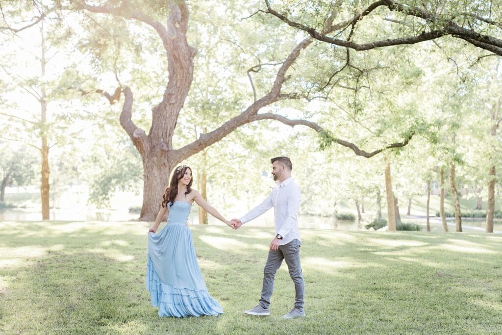 Bride walking through the pecan trees leading the groom for their engagement session at the orchard at caney creek