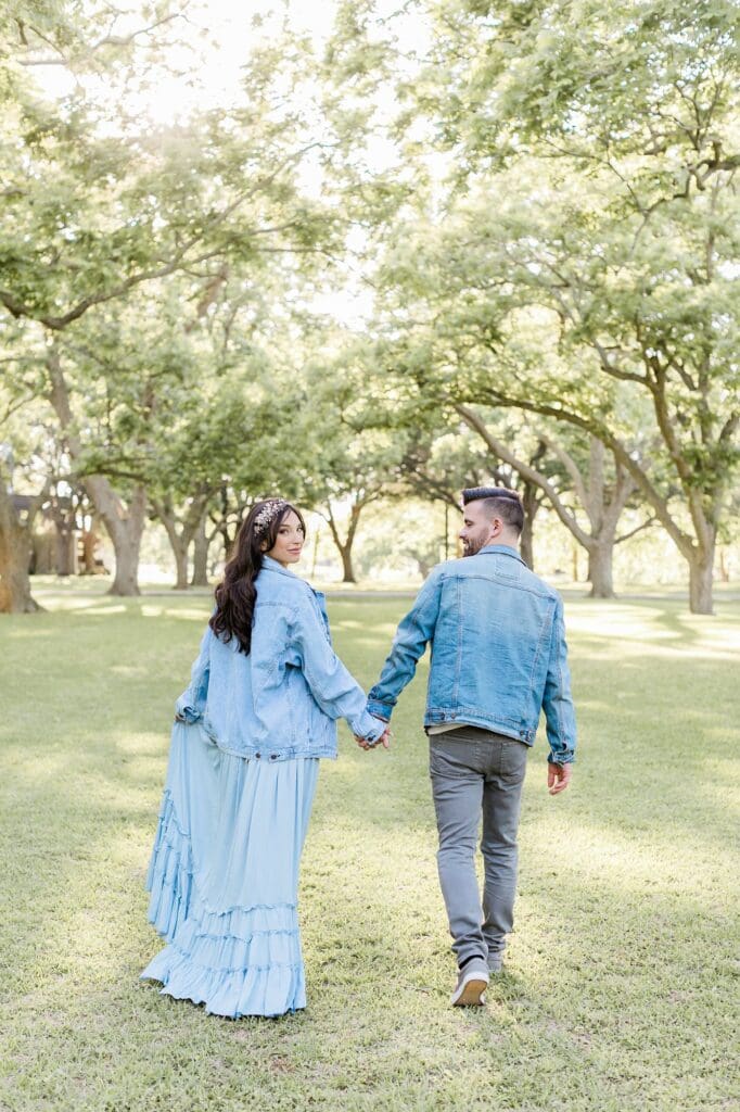 Bride looking back as her and the groom walk away under the pecan trees at their orchard at caney creek engagement session