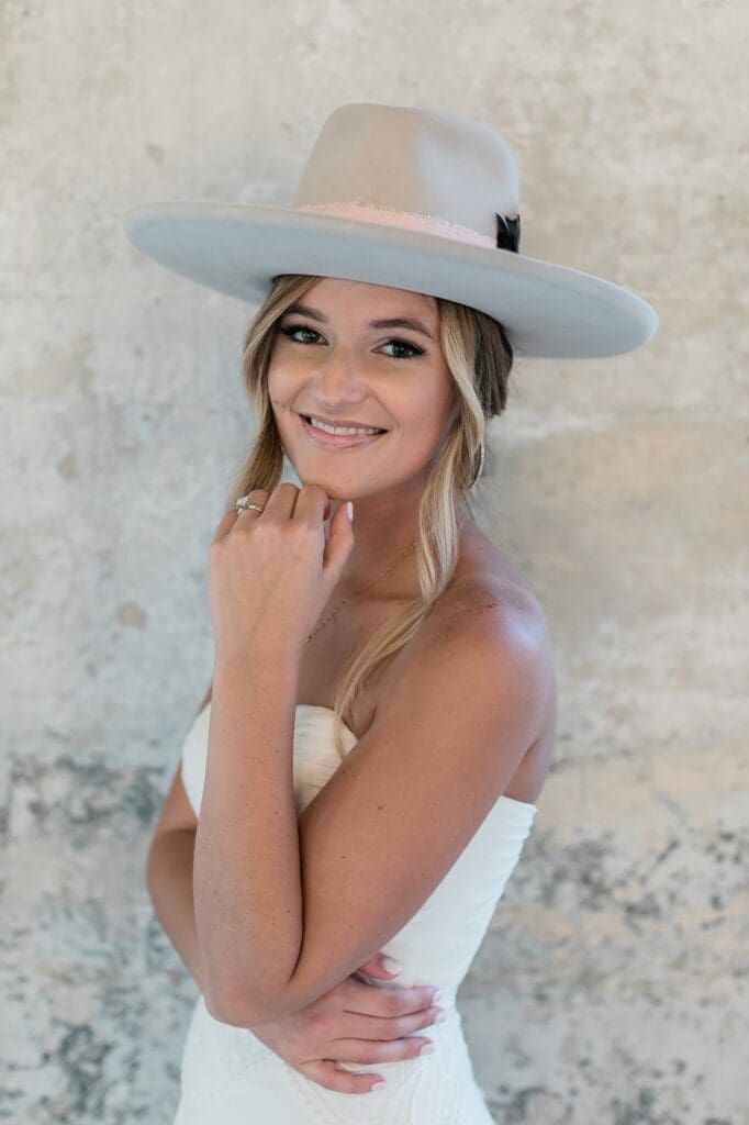 Bride smiling at the camera showing off her custom branded hat during her bridal portraits at Olde Dobbin Station