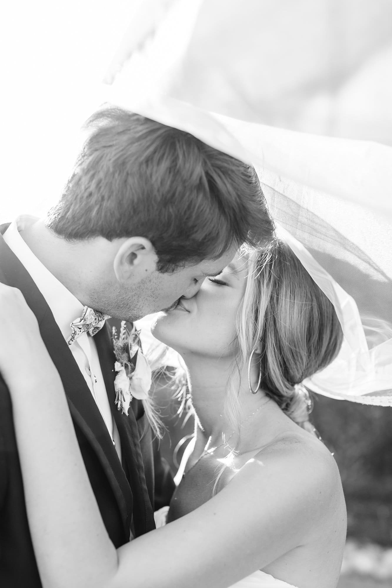 Black and white image of bride and groom kissing under the veil
