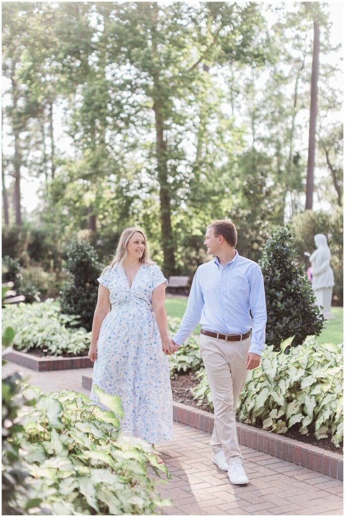 Alyssa and Ian walking through lush greenery at Mercer Botanic Gardens in Houston TX during engagement session