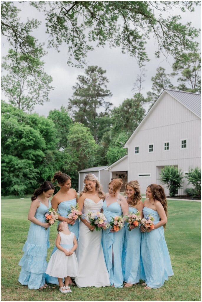 Bride and bridesmaids smiling at flower girl during bridesmaids portraits at Addison Woods
