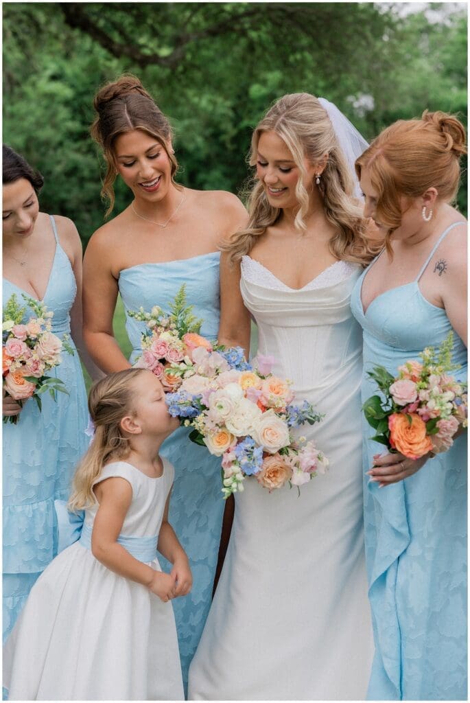 Flower girl smelling brides bouquet during bridesmaids portraits at Addison Woods 