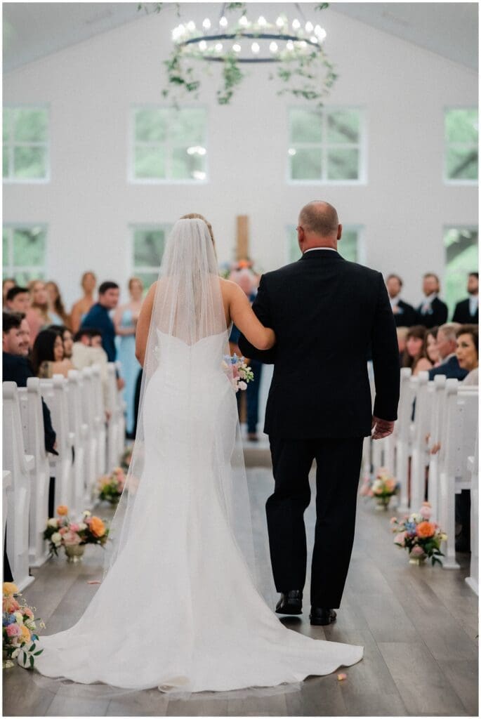 A shot from behind of the bride walking down the aisle with her father at Addison Woods
