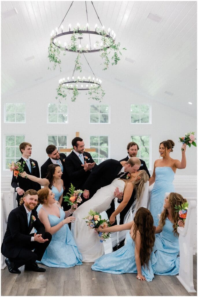Bride and groom kissing surrounded by wedding party cheering at Addison Woods