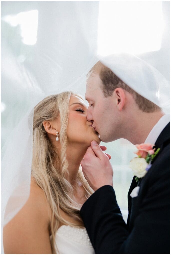 Bride and groom kissing under the veil at Addison Woods