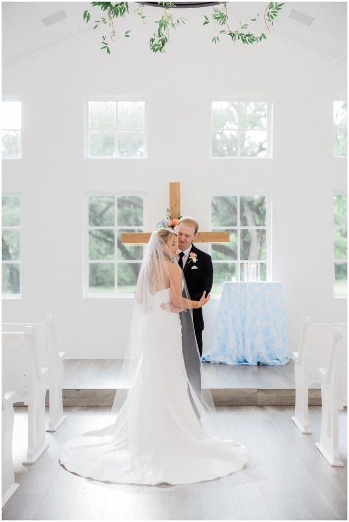 Bride and groom standing in front of the cross embracing at Addison Woods