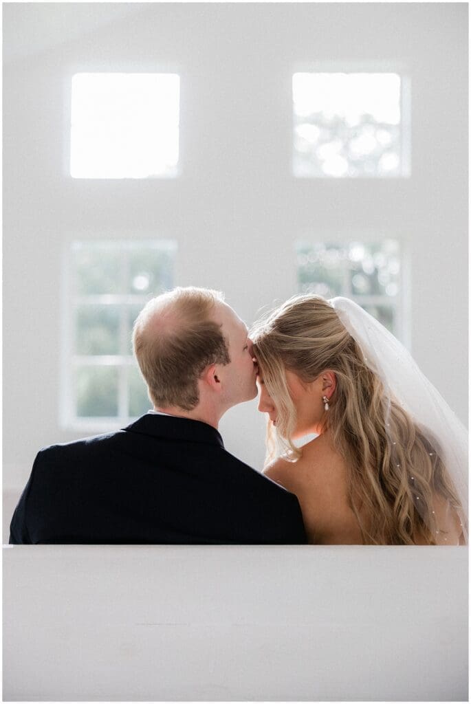 Groom kissing the brides forehead in the chapel pews at Addison Woods