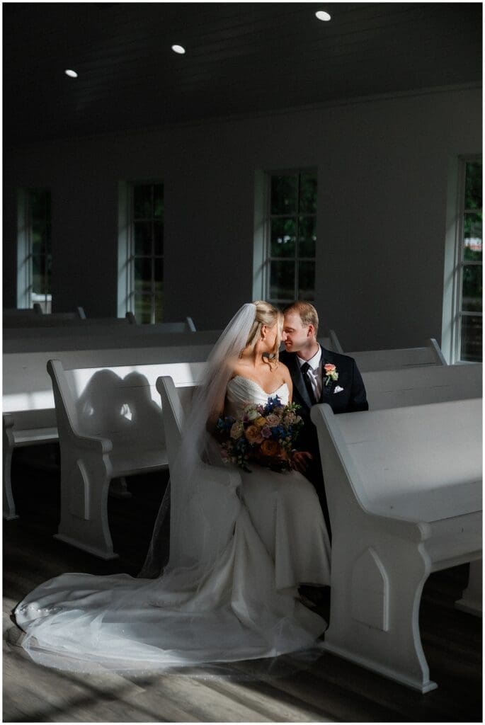 Sun casting on bride and groom sitting in the chapel pews at Addison Woods