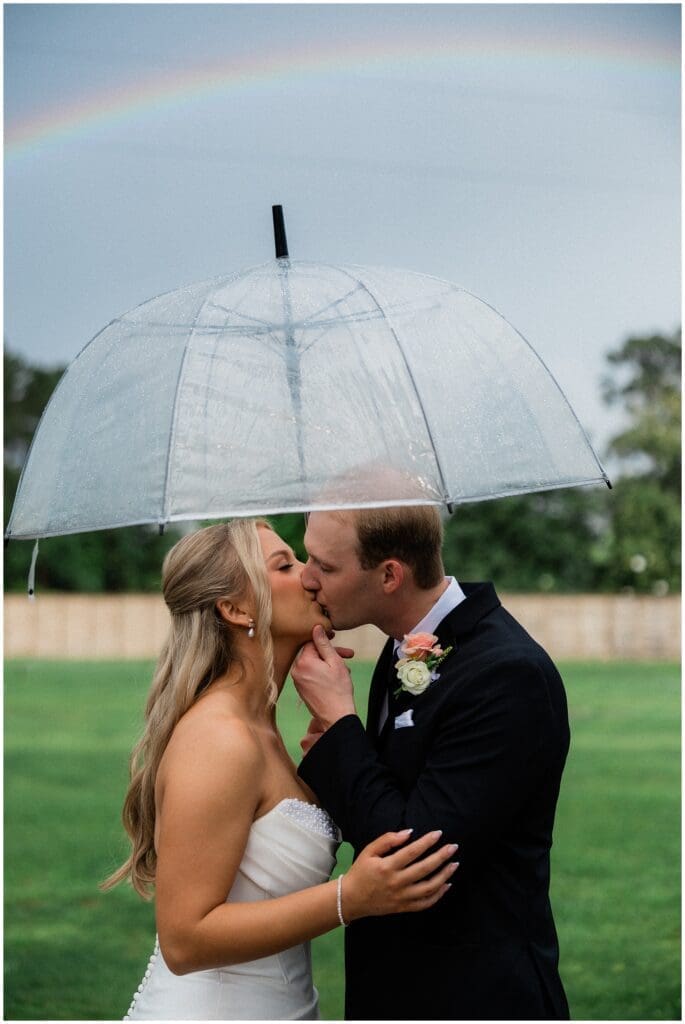 A rainbow on a rainy wedding day at Addison Woods while the couple kisses