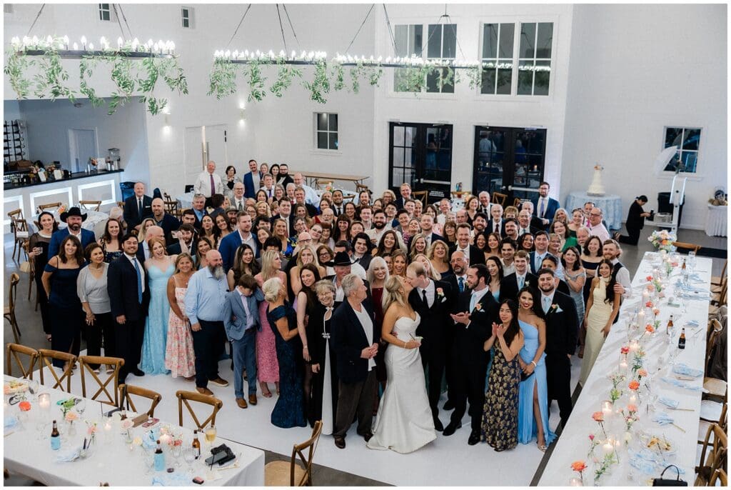 Bride and groom in a group picture with all their guests on the dance floor at Addison Woods
