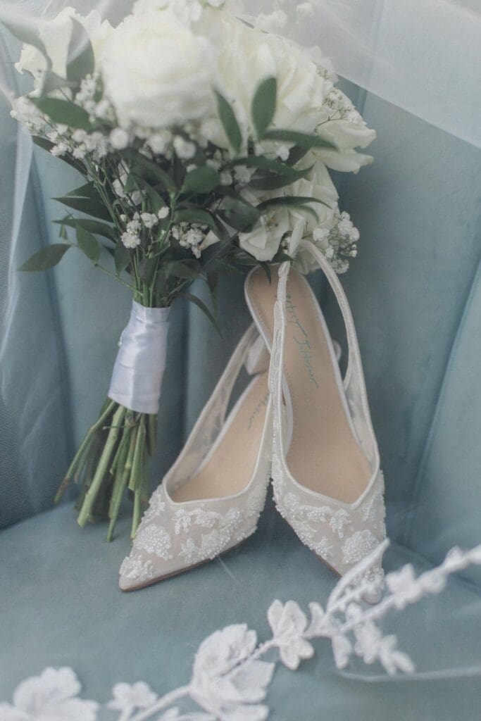 Bride's wedding shoes and bouquet sitting on a blue chair with a veil draped over it at iron manor
