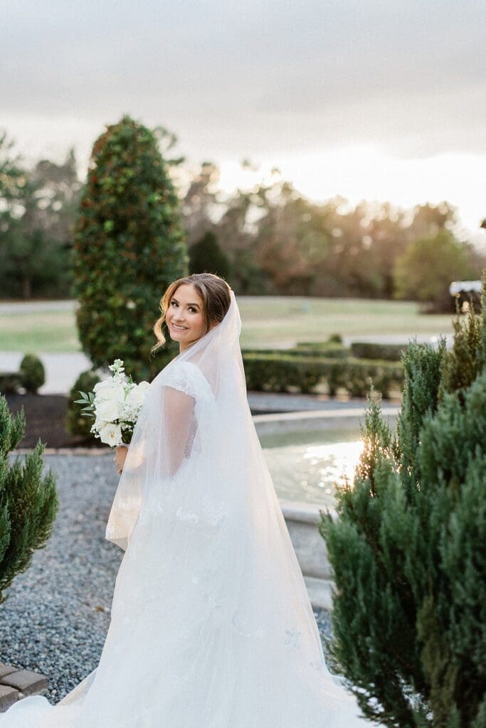 Bride looking back at the camera, standing in front of the fountain at Iron Manor for her golden hour bridal portraits