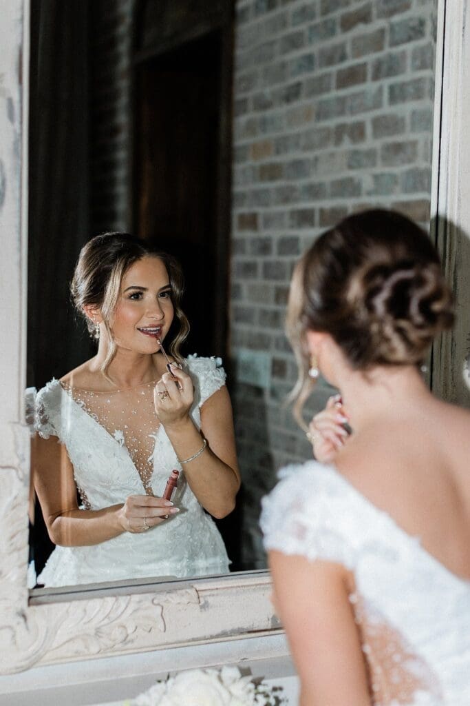 Direct flash of bride looking in the mirror doing her lipstick at Iron Manor