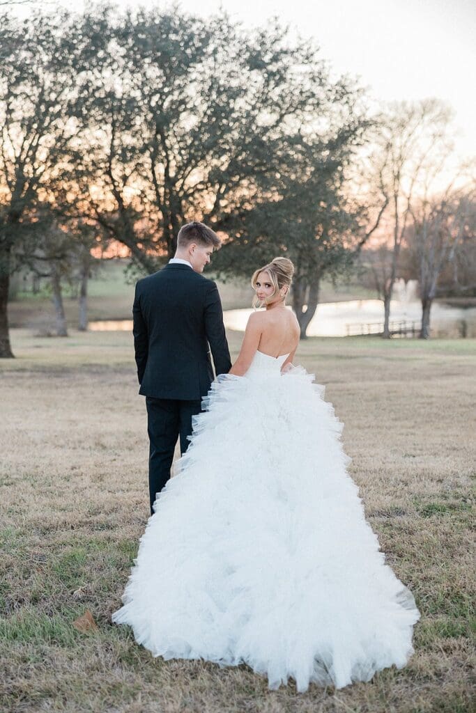 Bride looking back at the camera holding the grooms hand during their wedding at Aylin Acres